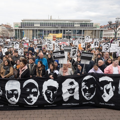 Menschen halten Bilder und Banner mit Gesichtern der Opfer von Hanau hoch