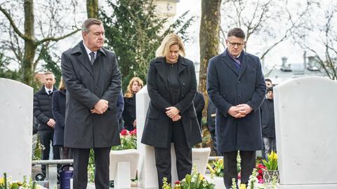 Claus Kaminsky (SPD, links), Oberbürgermeister von Hanau, Nancy Faeser (SPD), Bundesinnenministerin, und Boris Rhein (CDU), Ministerpräsident von Hessen, stehen auf dem Hanauer Hauptfriedhof zwischen Gräbern der Opfer. 