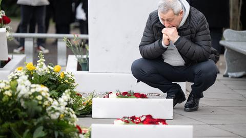 Ein trauernder Mann legt Blumen an einem Grab nieder.