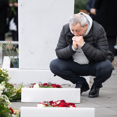 Ein trauernder Mann legt Blumen an einem Grab nieder.