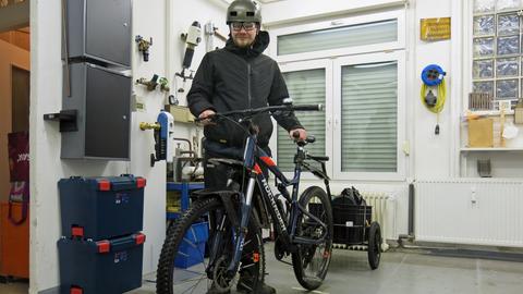 Mann mit Fahrradhelm steht in einer Werkstatt, seine Hände sind auf den Lenker eines Fahrrades.