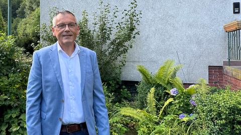 Landrat Andreas Siebert steht im Garten des Hauses. Er trägt ein mittelblaues Sakko, darunter ein hellblaues Hemd.