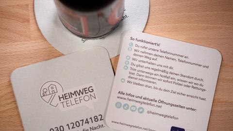 Bierdeckel mit Informationen zum Heimwegtelefon - Aufschrift: Sicher durch die Nacht und Telefonnummer 030/12074182