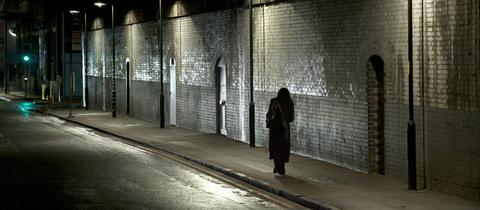 Eine Frau läuft nachts alleine durch die Straße. 