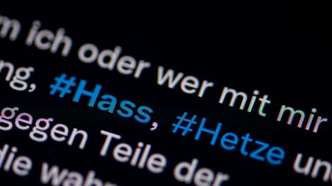 Der Bildschirm eines Smartphones zeigt die Hashtags #Hass" und #Hetze in einem Tweet.