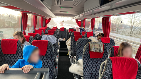 In einem zum Teil besetzten Reisebus sitzen einzelne Menschen, darunter auch Kinder.