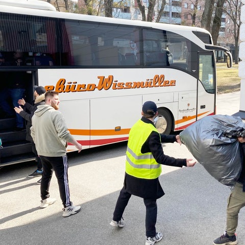 Ein Reisebus steht auf einem Parkplatz, eine Menschenkette lädt Kisten daraus aus.