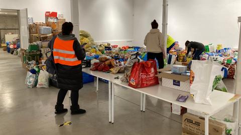 In einer Lagerhalle stapeln sich Kisten und Plastiktüten mit Hilfsgütern.