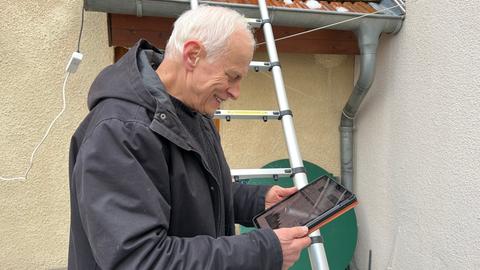Ein Mann steht vor einer Leiter und schaut auf ein Tablet.