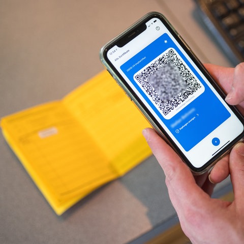 Gelber Impfpass und ein Smartphone mit QR-Code