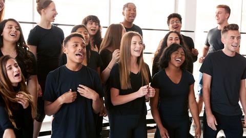 Foto: 15 junge Menschen singen zusammen. Alle tragen schwarze T-Shirts. Sie geben ein Konzert.
