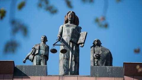 Drei Figuren auf dem Dach des Landgerichts Darmstadt. In der Mitte die blinde Justizia mit dem Richtschwert. Ihr zu beiden Seite zwei männliche Figuren. 