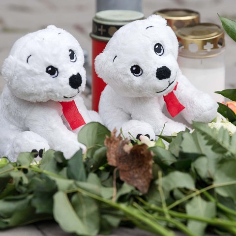Zwei Plüsch-Eisbären, Blumen und Grabkerzen in Großaufnahme.