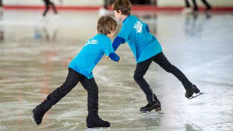 Zwei Kinder beim Schlittschuhlaufen in einer Eissporthalle