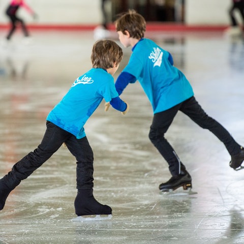 Zwei Kinder beim Schlittschuhlaufen in einer Eissporthalle
