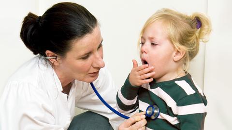 Kinderarzt untersucht Kind, Mutter lächelt