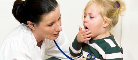 Eine Ärztin hält ein Stethoskop an die Brust eines Kindes, das hustet.