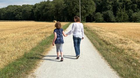 Nele und ihre Hospizbegleiterin Ruth Hopfenmüller gehen zwischen den Feldern Hand in Hand spazieren.