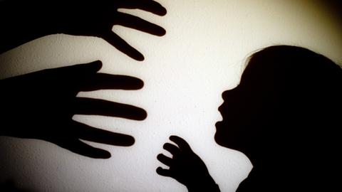 Schatten von Händen einer erwachsenen Person und der Kopf eines Kindes an einer Wand eines Zimmers