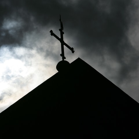 Kreuz auf Kirchendach unter bewölktem Himmel