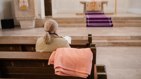 Eine Frau sitzt in einer Kirchenbank, über der eine Decke hängt.