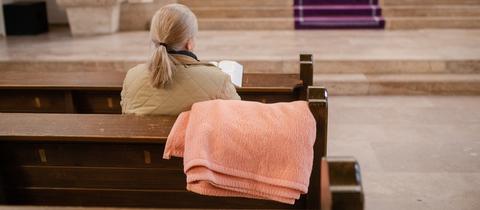 Eine Frau sitzt in einer Kirchenbank, über der eine Decke hängt.