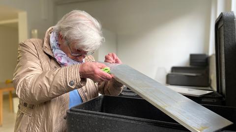 Eine ältere Frau begutachtet mit kritischem Blick die Sauberkeit einer Metallplatte.