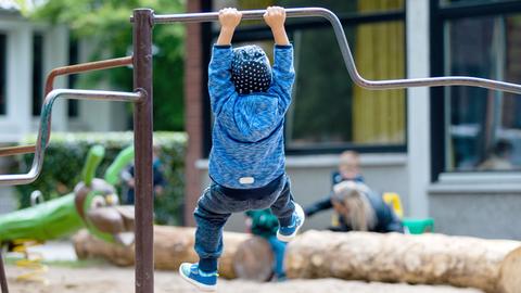 Ein kleines Kind hängt an einer Stange auf dem Spielplatz und lässt sich pendeln.