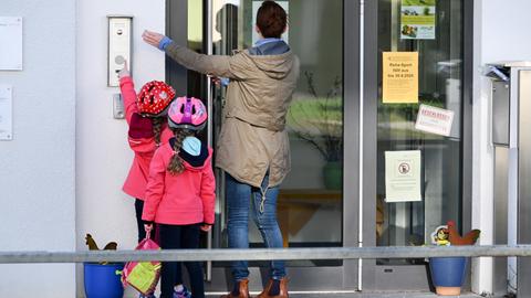 Mutter mit Kindern stehen vor und klingeln an einer Kita-Tür.