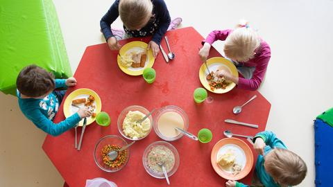 Kinder essen in einer Kita an einem Tisch zu Mittag.