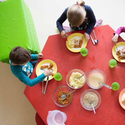 Kinder essen in einer Kita an einem Tisch zu Mittag.