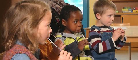 Kindersitzen auf Stühlen und haben mit Lolli-Tests in ihren Mündern.