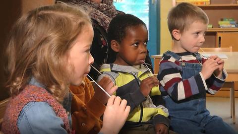 Kindersitzen auf Stühlen und haben mit Lolli-Tests in ihren Mündern.