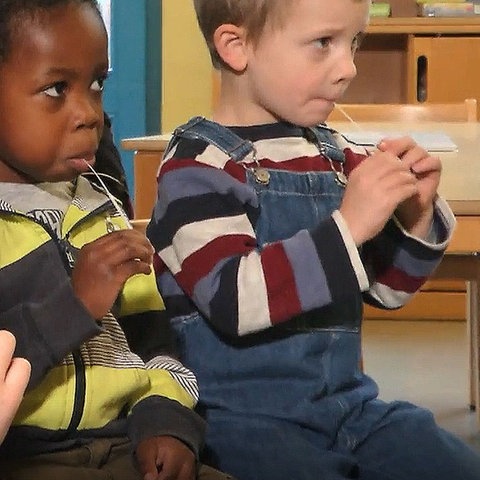 Kindersitzen auf Stühlen und haben mit Lolli-Tests in ihren Mündern.