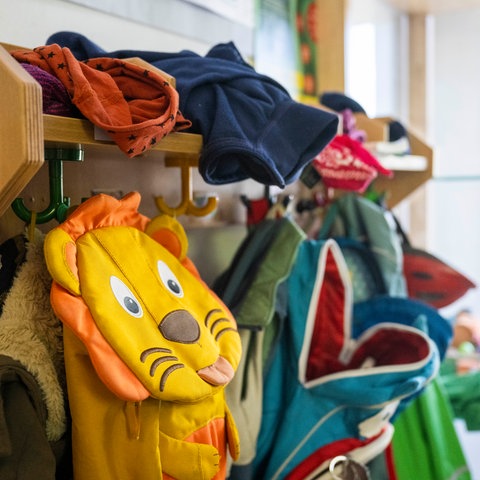 In einer Garderobe einer Kindertagesstätte hängen bunte Rucksäcke und Jacken.