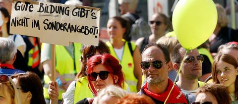 Menschenmasse mit Frauen und Männern mit gelben Westen. Eine Frau hält ein Schild mit dem Text "Gute Bildung gibt es nicht im Sonderangebot". 