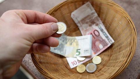 Körbchen mit Geld auf Kirchenbank, eine Hand hält eine Münze