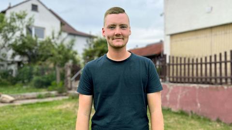 Konstantin Sauer steht in einem Garten mit Haus im Hintergrund und schaut in die Kamera.