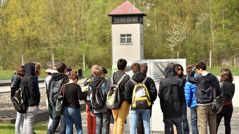 Eine Gruppe von Jugendlichen steht auf einem Platz in einem ehemaligen Konzentrationslager, im Hintergrund ein Wachturm