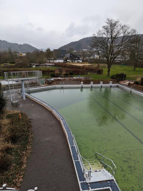 Sprungtürme vor grünlichem Freibad-Becken im Regen