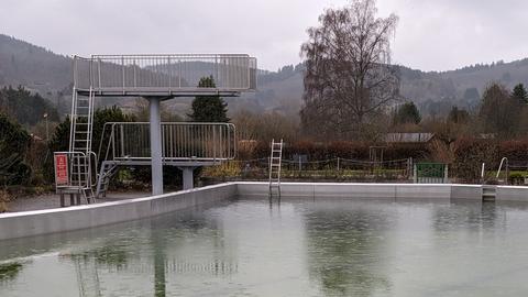 Sprungtürme vor grünlichem Freibad-Becken im Regen