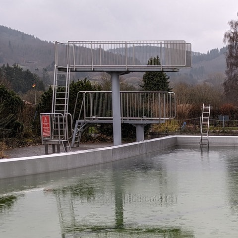 Sprungtürme vor grünlichem Freibad-Becken im Regen