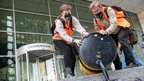 Zwei Menschen kippen ein Fass mit schwarzer Flüssigkeit draußen auf einer Treppe aus