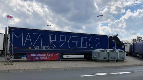 Ein blauer Lkw, auf dessen Plane des Aufliegers man die Schuldensumme 97.585 Euro geschrieben hat