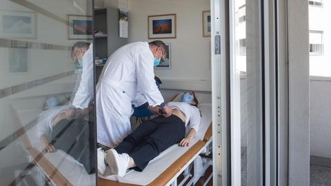 Ein Arzt behandelt eine Long-Covid-Patientin, die auf einer Liege liegt.