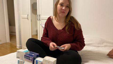 Long-Covid-Patientin Sofie Jankuhn auf ihrem Bett mit einer Schachtel voller Medikamente