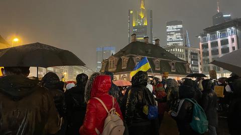 Eine Menschengruppe steht zwischen Hochhäusern, eine gelb-blaue Flagge ist zu sehen.