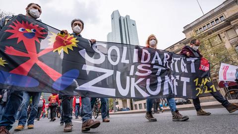 1.Mai in Frankfurt: Menschen mit einem Transparent mit dem Motto "Solidarität ist Zukunft" laufen an der Zentrale der Deutschen Bank vorbei.