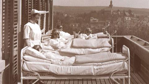 Historische Schwarz-Weiß-Aufnahme von Kindern, die in Krankenbetten auf einem Balkon liegen