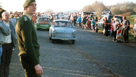 Ein Soldat der Bundeswehr und viele Einwohner von Kleinensee stehen am 12. November 1989 am geöffneten Grenzübergang zwischen Wildeck-Obersuhl und Gerstungen am Straßenrand, während Trabis vorbeifahren